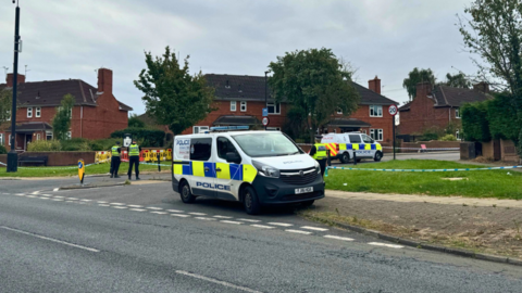 Police officers and van stationed in front of a blue and white cordon at the top of Bellfarm Avenue 