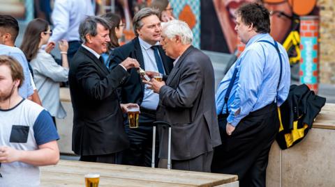 Group of many businessmen people standing outside in England at the Shipwrights Arms pub tavern bar drinking beer from cups