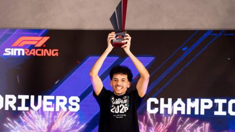 Otis Lawrence holding a trophy in the air. He is smiling. Otis has short dark hair and short stubble, and is wearing a black t shirt with the Words World Champion 2026 written on it.
