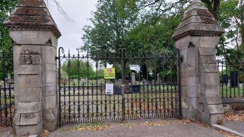 The cemetery gates with a lock around them and a note explaining the reason for the closure