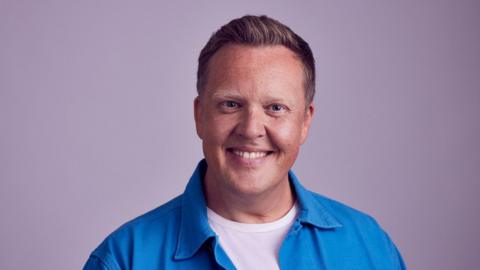 A man wearing a blue shirt smiles at the camera