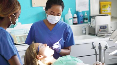 Young female dentist and assistant working on female patient in chair