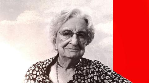 An elderly woman wearing a flowery top looks at the camera