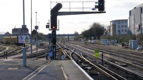 Multiple rail tracks at Eastleigh with speed signs and gantry with lights lit overhead.