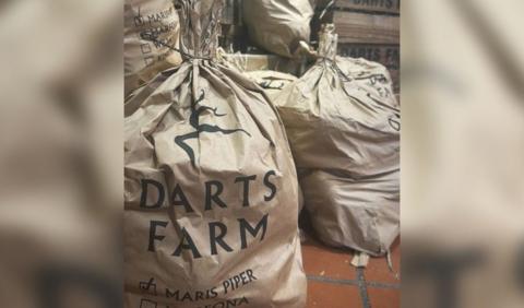 Several bags of potatoes with a green Darts Farm logo printed on the side.