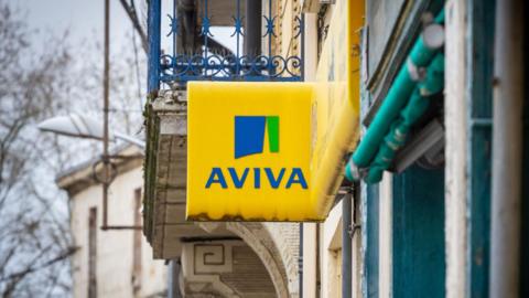 A yellow Aviva signs hangs outside a building on a grey skied day