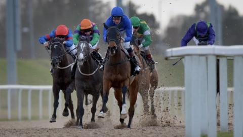 Jockeys wearing colourful racing silks riding their horses along the track in Chelmsford.