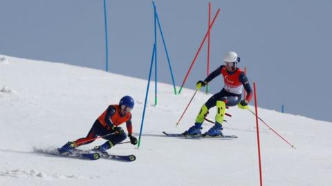 Great Britain's Neil Simpson competes in the alpine skiing with his guide Andrew who is skiing in front of him between poles down a snowy hill