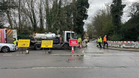 A road closed sign with a SGN tanker and fences blocking the road