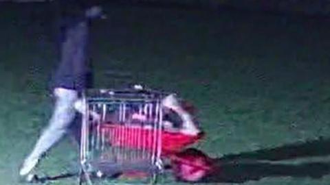 CCTV footage of a person in a dark hooded top pushing a wheel barrow filled with stuff across a field