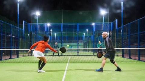 Four people play the game on a court. They are wearing different coloured sportswear and their rackets are black.