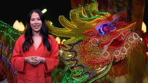 Reporter Liz Clements in front of a Chinese New Year carnival backdrop