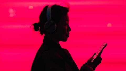 Silhouette of someone wearing headphones looking at their phone