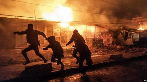 Group of people running with large fire in background