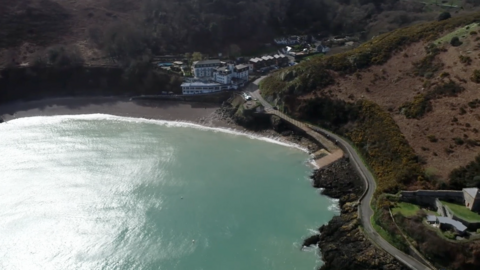 a high up shot of bouley bay - the sea beside a road and lots of woodland