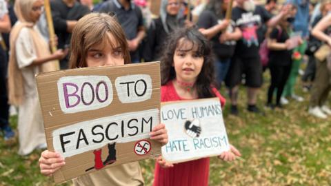 Two young girls holding placards- boo to fascism and love humans hate racism 