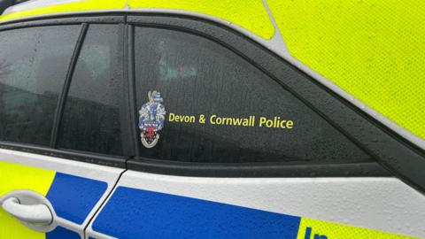 A close up of the side of a yellow and blue Devon and Cornwall Police car.