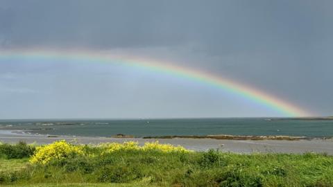 Rainbow stretches across the horizon with sea and land in front 