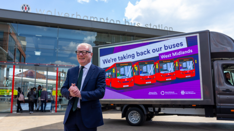 Parker is stood outside Wolverhampton bus station with a van advertising the new franchise system. It depicts red buses with a strapline above that says: We're taking back our buses