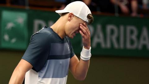 Holger Rune holds his hand over his eyes as he walks off the court with injury
