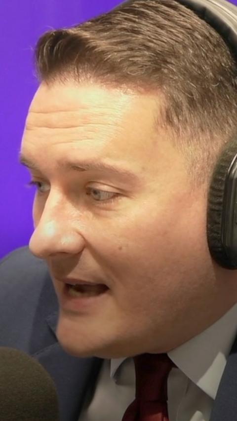 A man with short cropped brown hair wears headphones and talks into a microphone