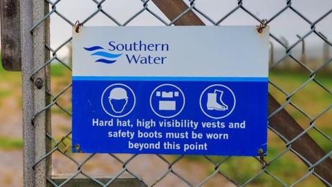A blue and white Southern Water sign on a metal fence.