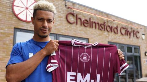 Lyle Taylor holding a Chelmsford City shirt