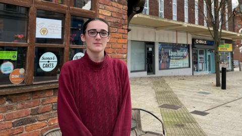 A woman stands in front of her cafe and looks at the camera