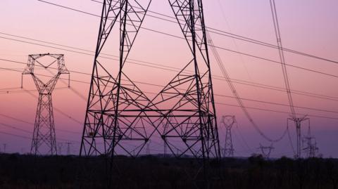 The outline of electricity pylons with a pink sunrise in the background.