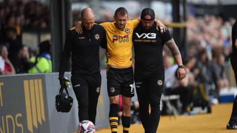 Newport County's Shane McLoughlin is helped off the pitch by coaching staff after injury