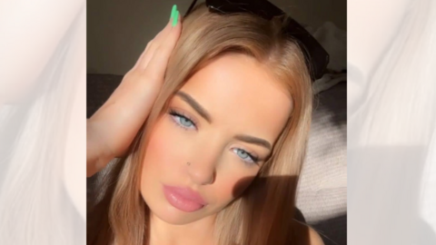 A young woman with blonde hair and sunglasses on her head poses for the camera as she takes a selfie, with the shadow of her phone seen on her cheek.