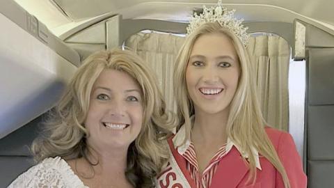 Close up of Vicky and Tabitha Bennett on an aeroplane. Both are blonde and smiling, Vicky's hair is wavy and Tabitha's is straight and she is wearing a tiara
