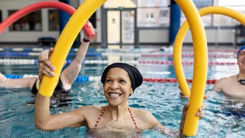 Healthy senior woman doing swim noodle exercises in aerobics pool class 
