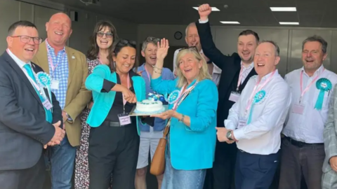 The new group of Reform UK councillors pictured after their emphatic win at the May local elections. A group of 10 people are in the picture, with two councillors in the middle cutting a cake.