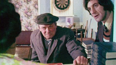Charlie Large wearing a flat cap leaning over a counter in a pub
