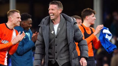 Rob Edwards smiling with Luton players wearing orange behind him