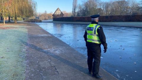 Police officer standing next to a frozen pond in Rowntree Park, York