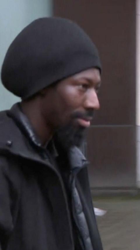 Charles Brohiri leaving court wearing a large dark-coloured hat