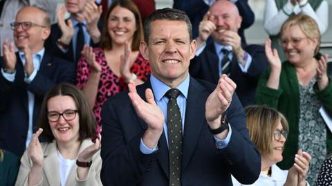 Rhun ap Iorwerth applauding on the steps of the Senedd building steps