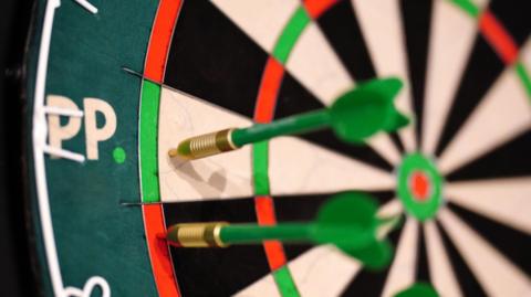 A close up view of part of a darts board. Two green darts rest in the board.