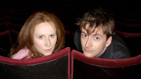 Catherine Tate and David Tennant looking back at the camera from cinema seats