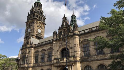 The outside of Sheffield Town Hall. It is a Grade I listed building, in a gothic Victorian style with a clock tower, turrets and large arched windows.