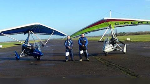 Two men seen standing in front of microlight aircraft