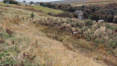 A dry pond known as an attenuation basin on the hillside at Annabut Lee Farm above Cragg Vale, that fills during heavy rainfall.