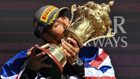 Lewis Hamilton kisses the trophy with a Union flag draped over his shoulders after winning the 2024 British Grand Prix