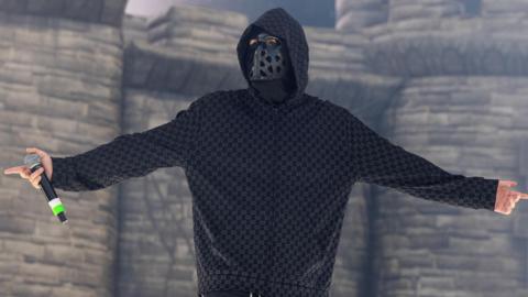 EsDeeKid performs in front of a blow-up castle during a set in Illinois. He is seen looking at the crowds while holding a microphone and wearing a black mask with holes and a hoodie.