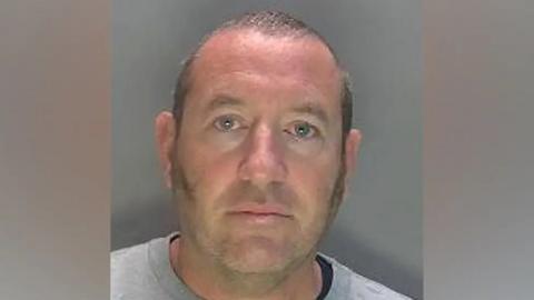 David Carrick mugshot - staring at camera, man with sideburns