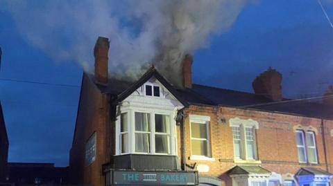 An image of a row of houses with smoke seen billowing from the top of an end-terrace property