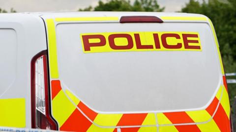 A general view of a police van. The van is white with orange and yellow trim. It has the word 'Police' on in red writing against a yellow background. 