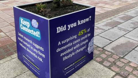 A plant box on a town centre pavement has purple hoardings from Dementia Jersey around it as part of the charity's Boost Your Brain campaign. The hoardings have text on them saying 45% of dementia cases could be avoided with simple lifestyle changes.